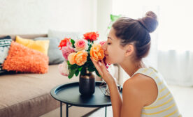Woman smelling fresh roses in vase on table. Housewife taking care of coziness in apartment. Interior and decor
